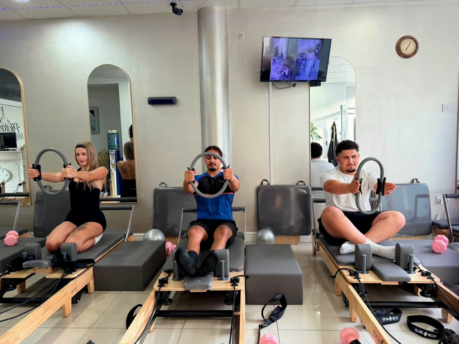 Three clients seated on Reformers pressing a Pilates ring at chest height